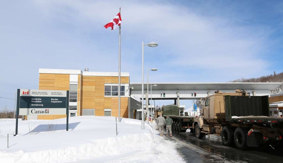 US Army Reserve trucks cross under an overhang at the Canadian border in winter.