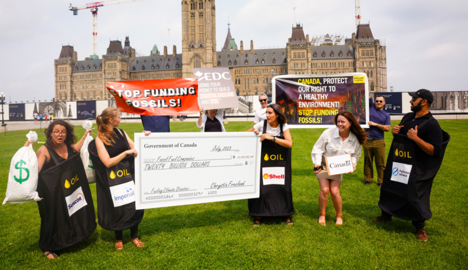 Nine activists on Parliament Hill hold signs calling on the Canadian government to stop funding fossil fuels