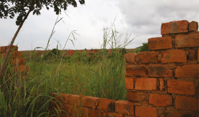 Grass grows around the remains of a orange brick wall on an overcast day
